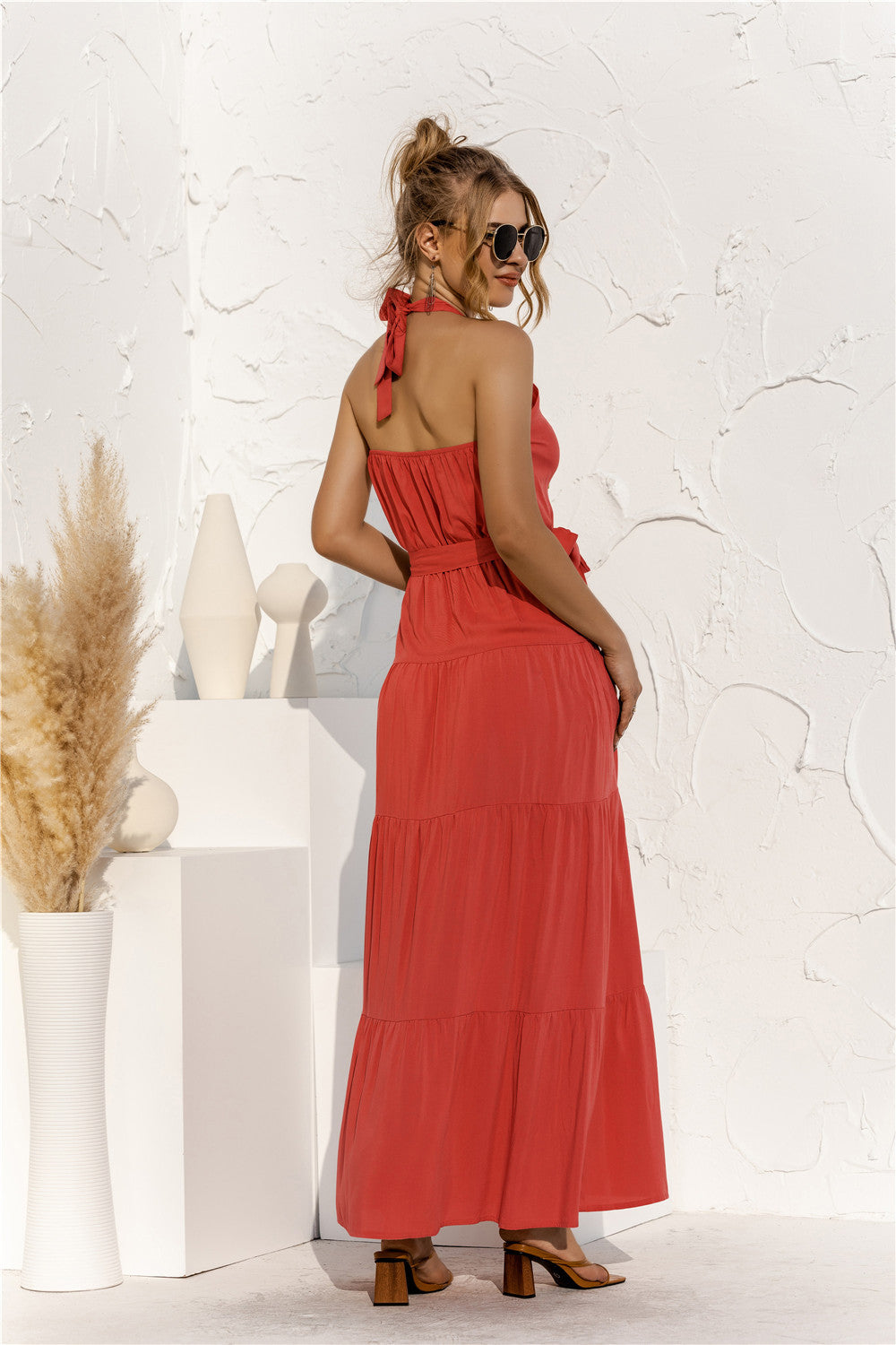 Model back view wearing orange halter neck tiered maxi dress with tie front waist in the color orange.
