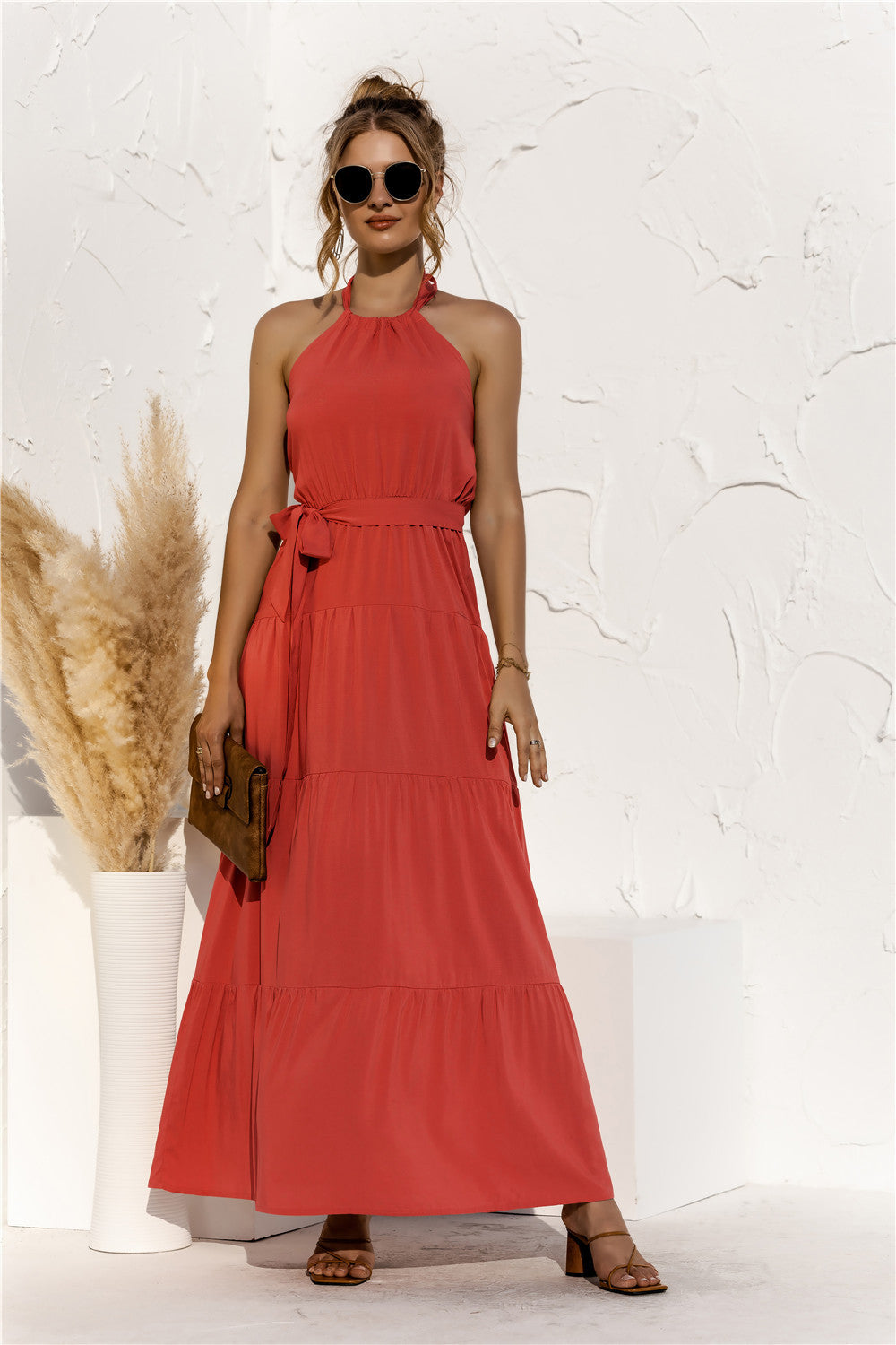 Model is wearing a orange halter neck tiered maxi dress with tie front waist in the color orange. 
