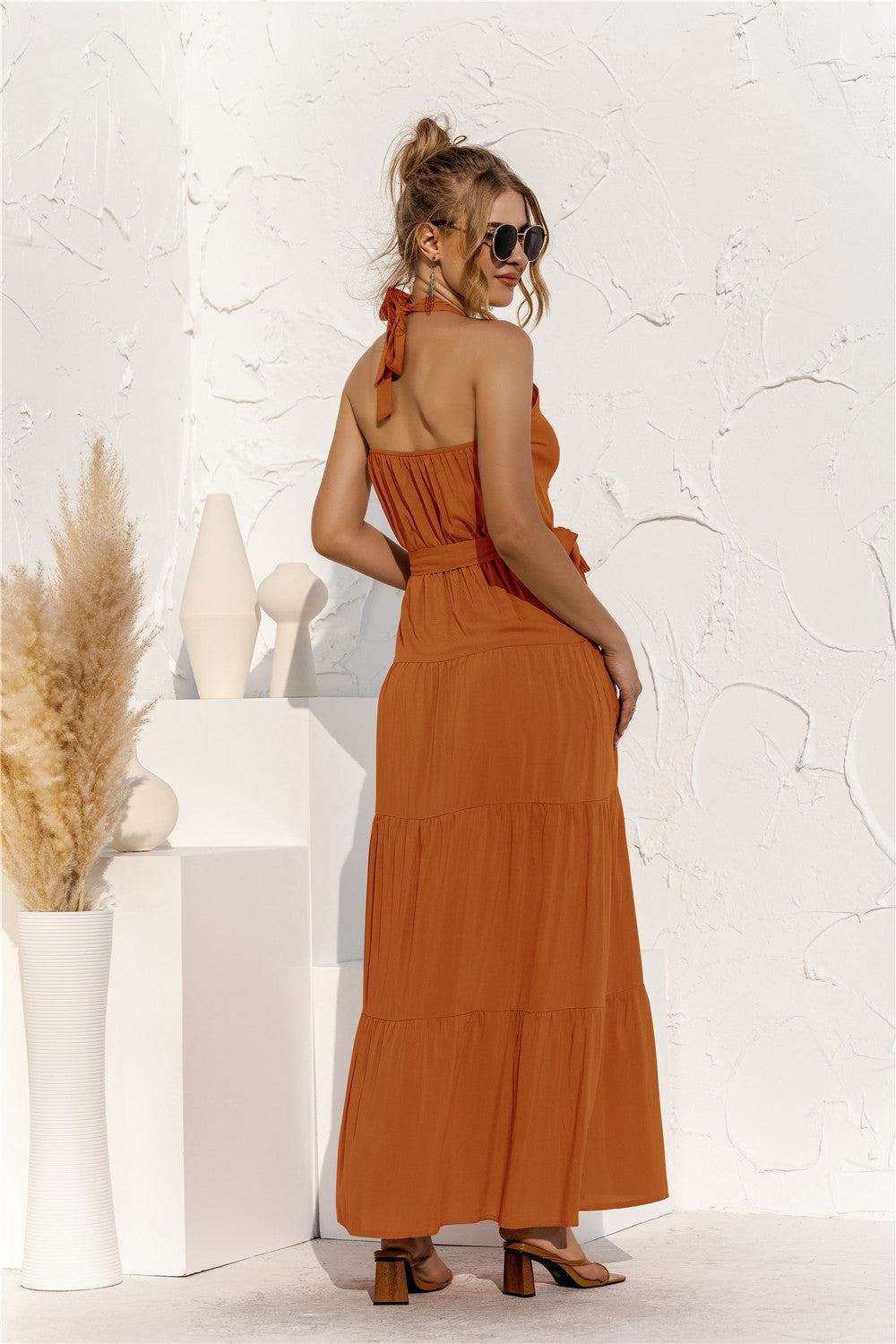 Back view of model wearing halter neck tie maxi dress with tie front waist in the color terracotta.