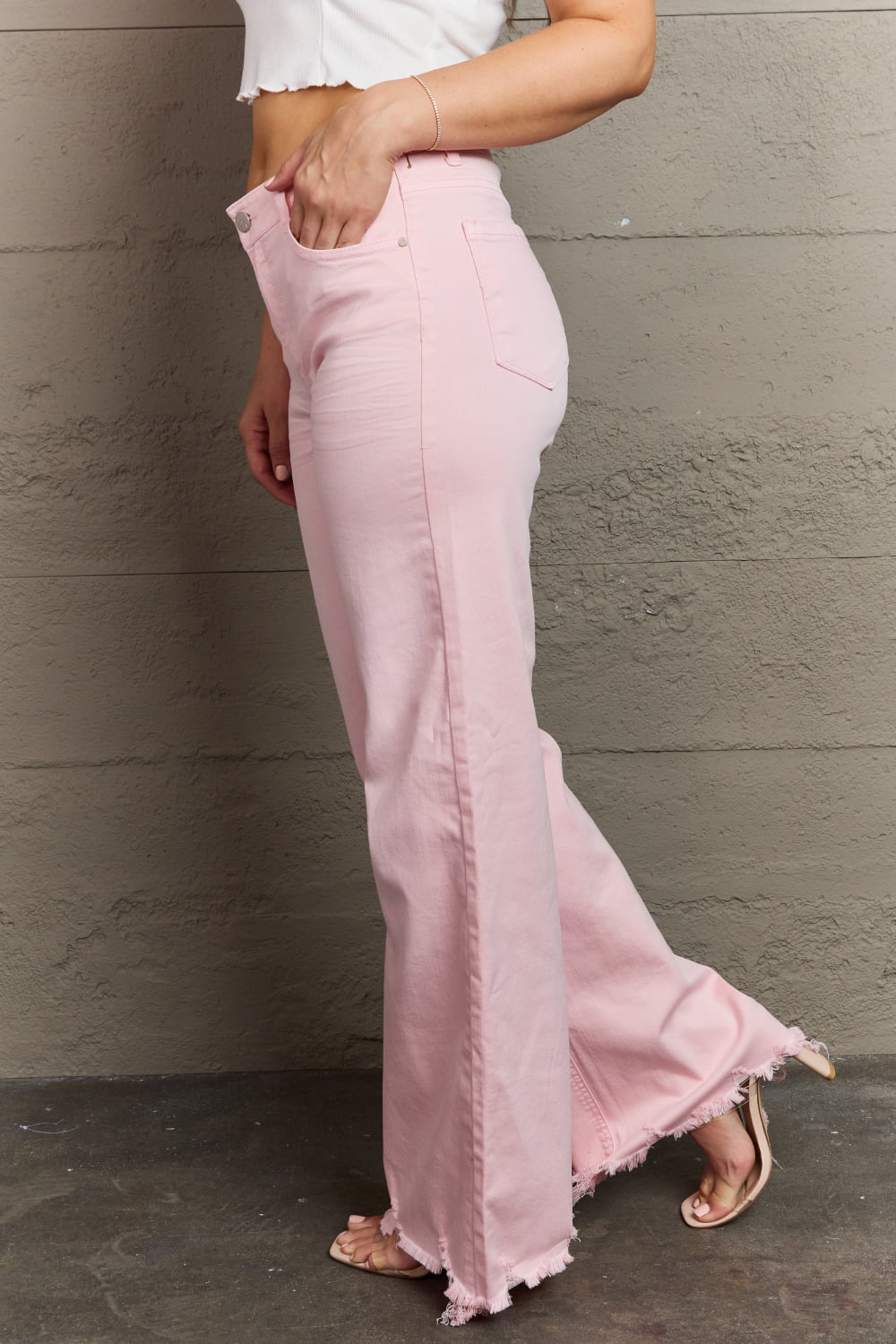 Side view of model wearing RISEN Raelene Full Size High Waist Wide Leg Raw Hem Jeans in Light Pink