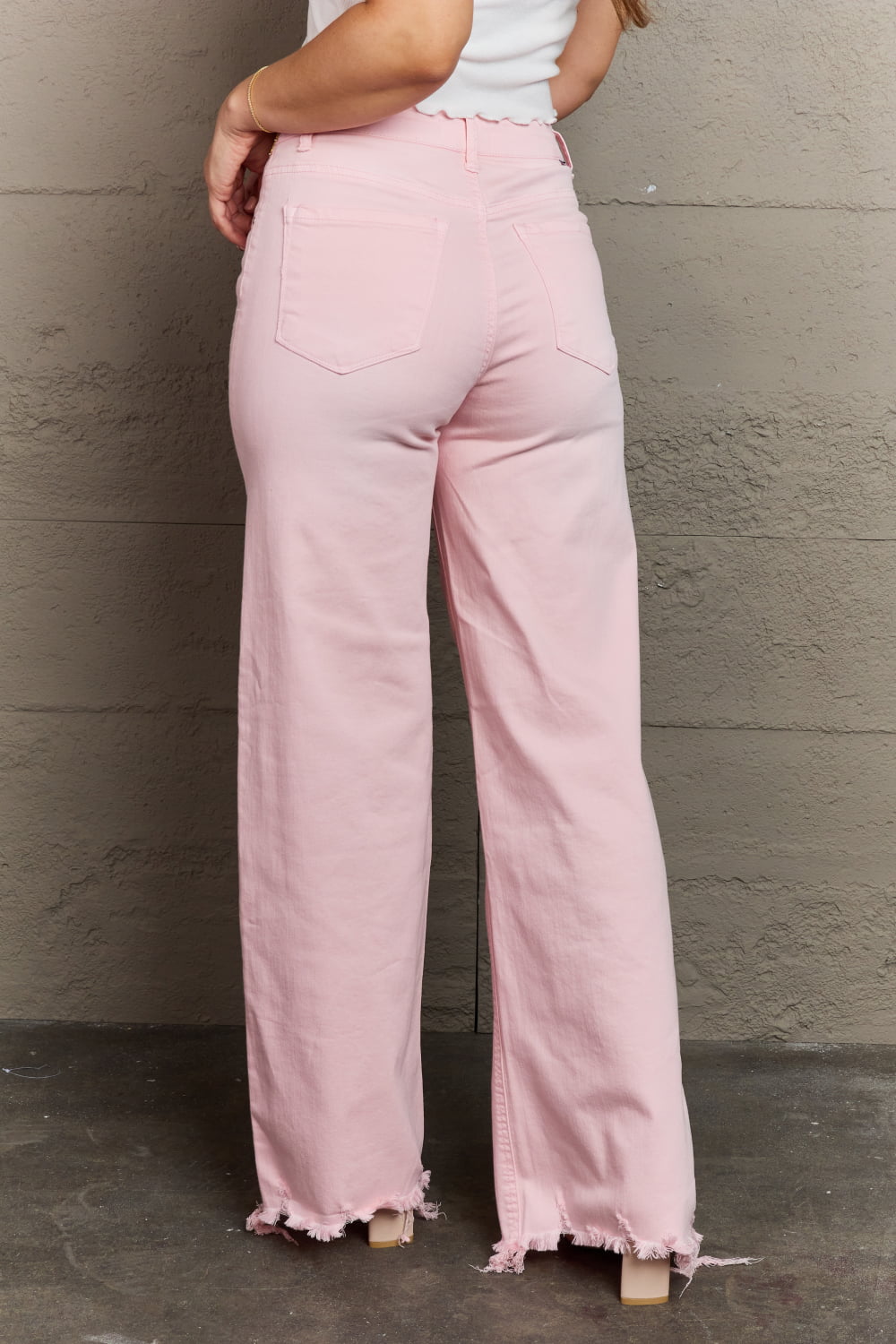 Back view of model wearing RISEN Raelene Full Size High Waist Wide Leg Raw Hem Jeans in Light Pink