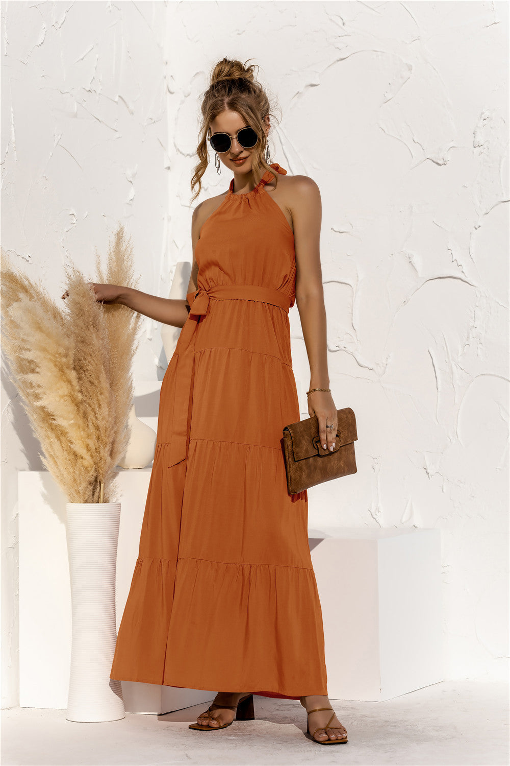 Model front view wearing halter neck maxi dress with tie front waist in the color terracotta.